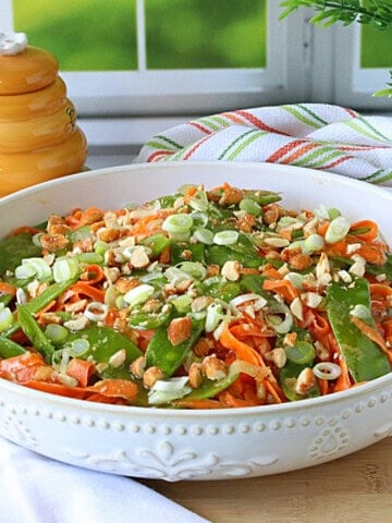 Orange shredded carrots and green snow peas mixed together in a white bowl.