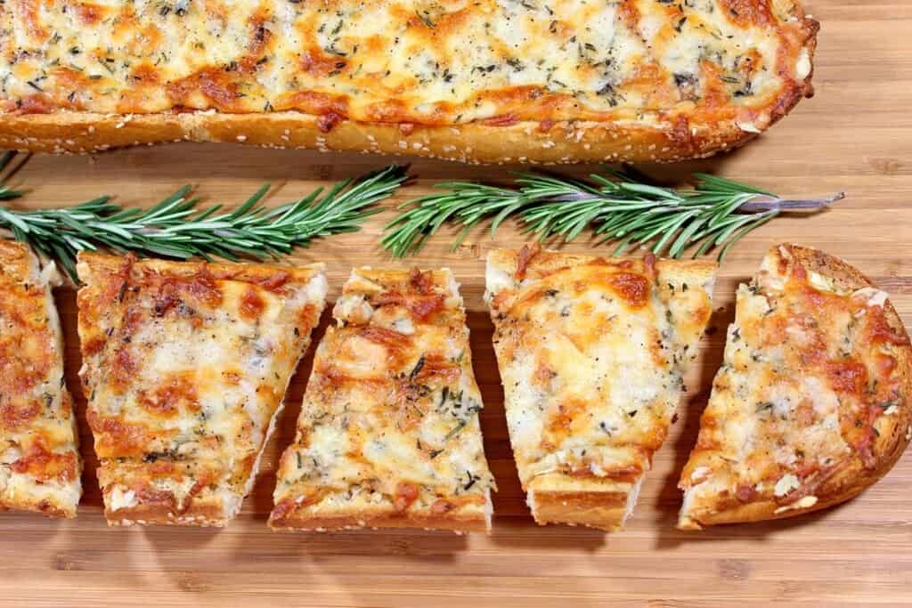 Two toasted Garlic Cheese Bread Loaves on a wooden cutting board with a sprigs of rosemary inbetween.