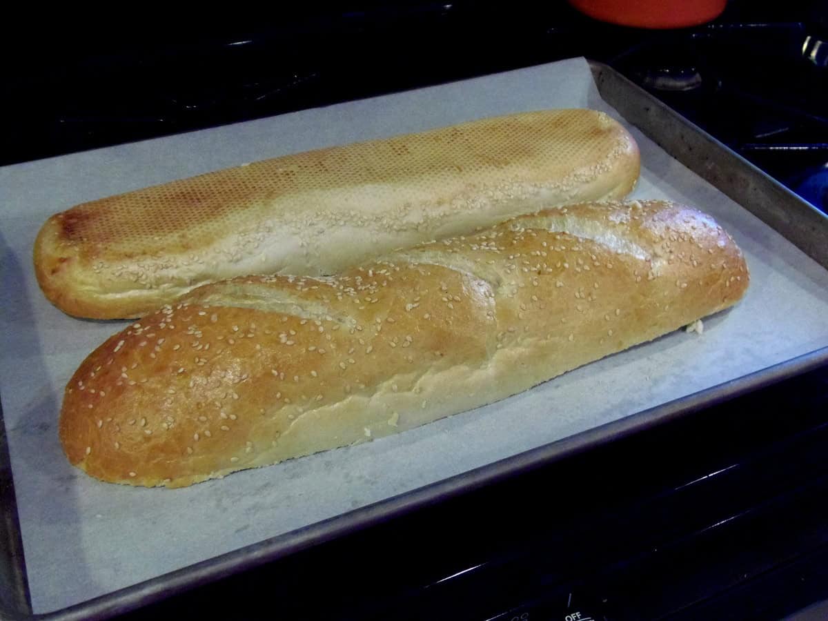 A fresh loaf of Italian bread that's been sliced in half and placed sliced-side down on a baking sheet.
