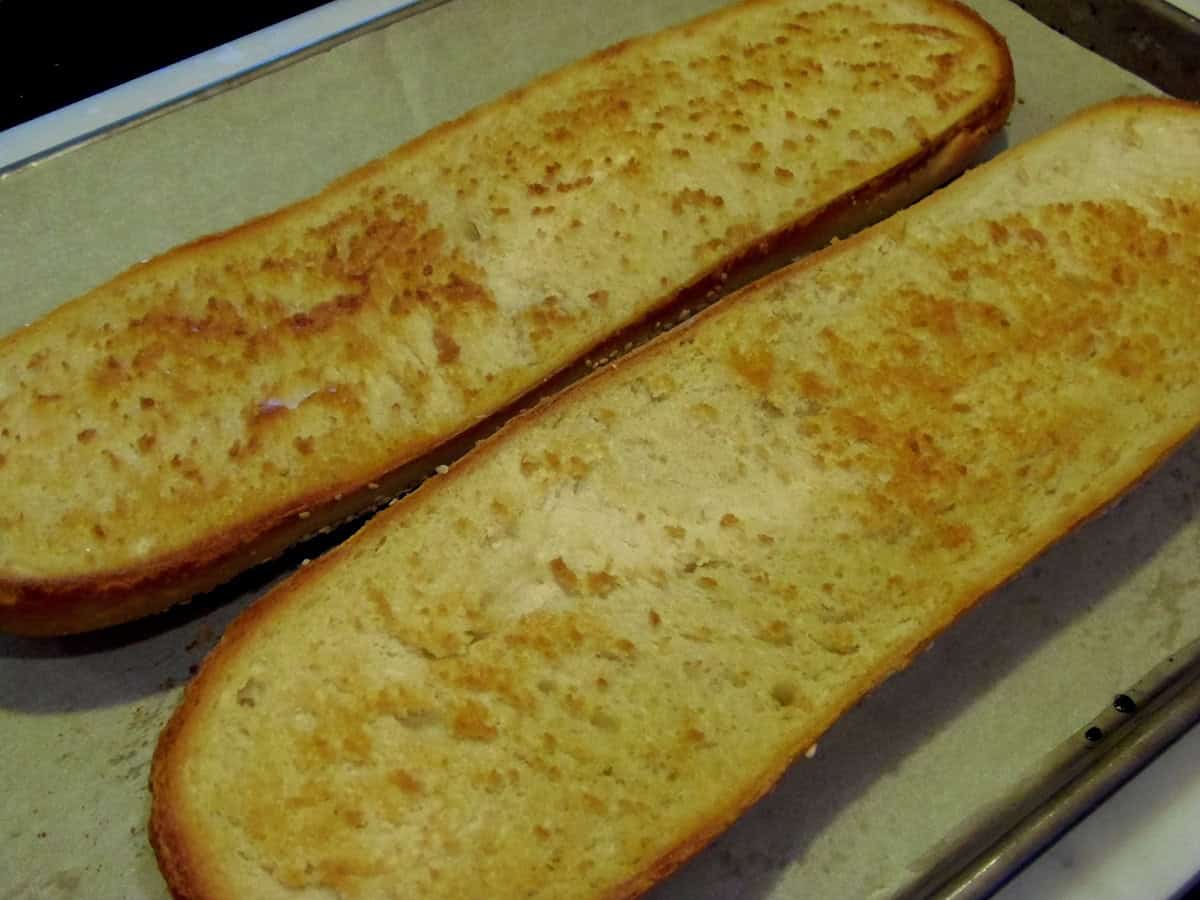Toasted, golden brown Italian bread that's been cut in half on a baking sheet.