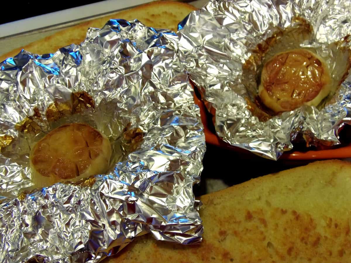 Two golden brown bulbs of garlic in foil packets after roasting and ready to use.