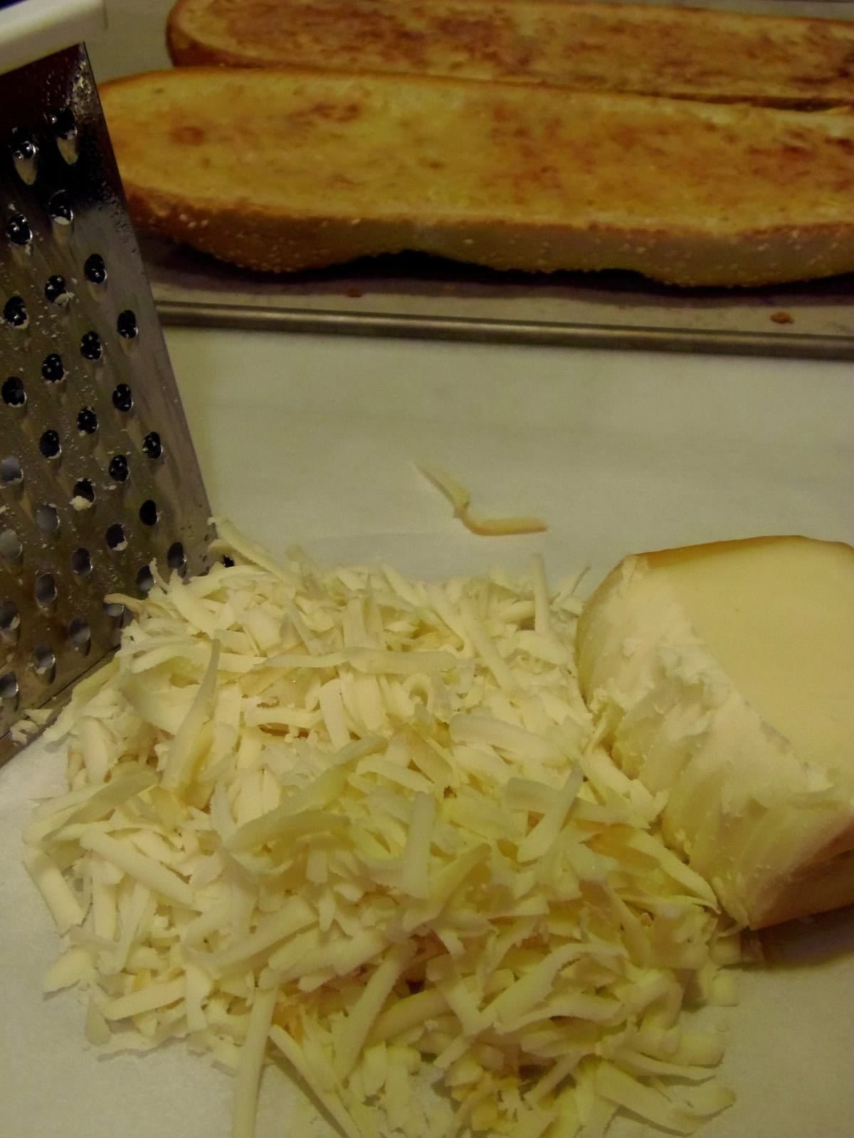 A box grater next to a pile of shredded smoked mozzarella cheese.