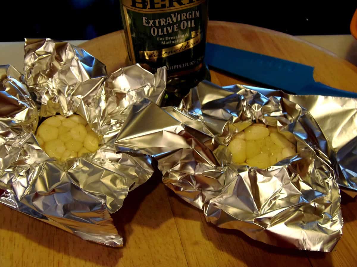 Two bulbs of garlic drizzled with olive oil and wrapped in foil ready for roasting.