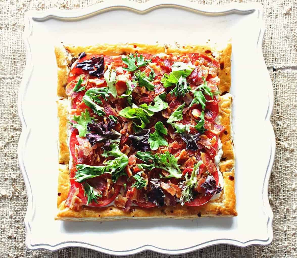 Whether you serve this delectable BLT Puff Pastry Tart with a Balsamic Drizzle for an appetizer or main course, you're going to love the fresh tomato flavor topped by oodles of crispy, smoked bacon. - Kudos Kitchen by Renee A pretty square of BLT Puff Pastry Sandwich Tart before slicing.