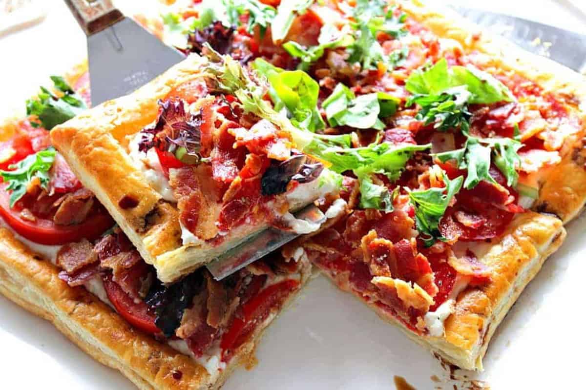 A serving of a savory BLT Puff Pastry Sandwich Appetizer Tart on a square serving spatula.