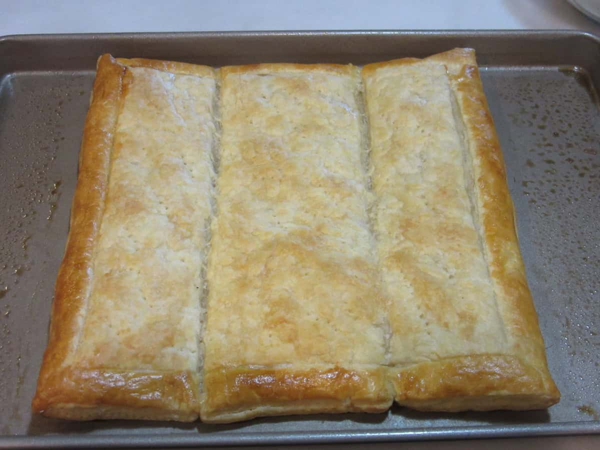 A puffed square of baked puff pastry dough with a golden frame after being egg washed.