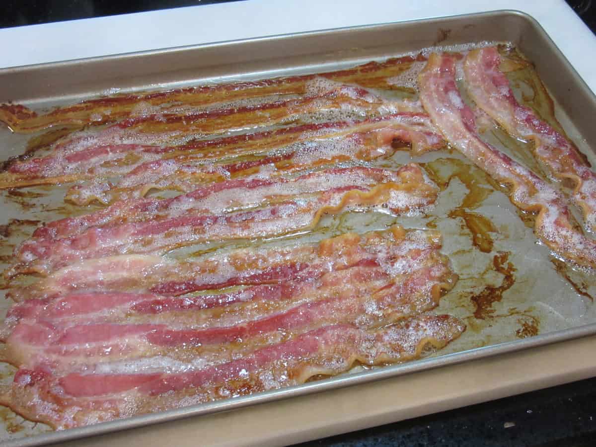 Strips of cooked bacon on a baking sheet after being taken out of the oven.