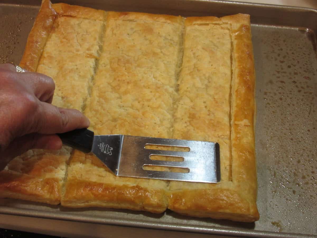 A square spatula pressing down the inside of a baked puff pastry square to make room for the filling.