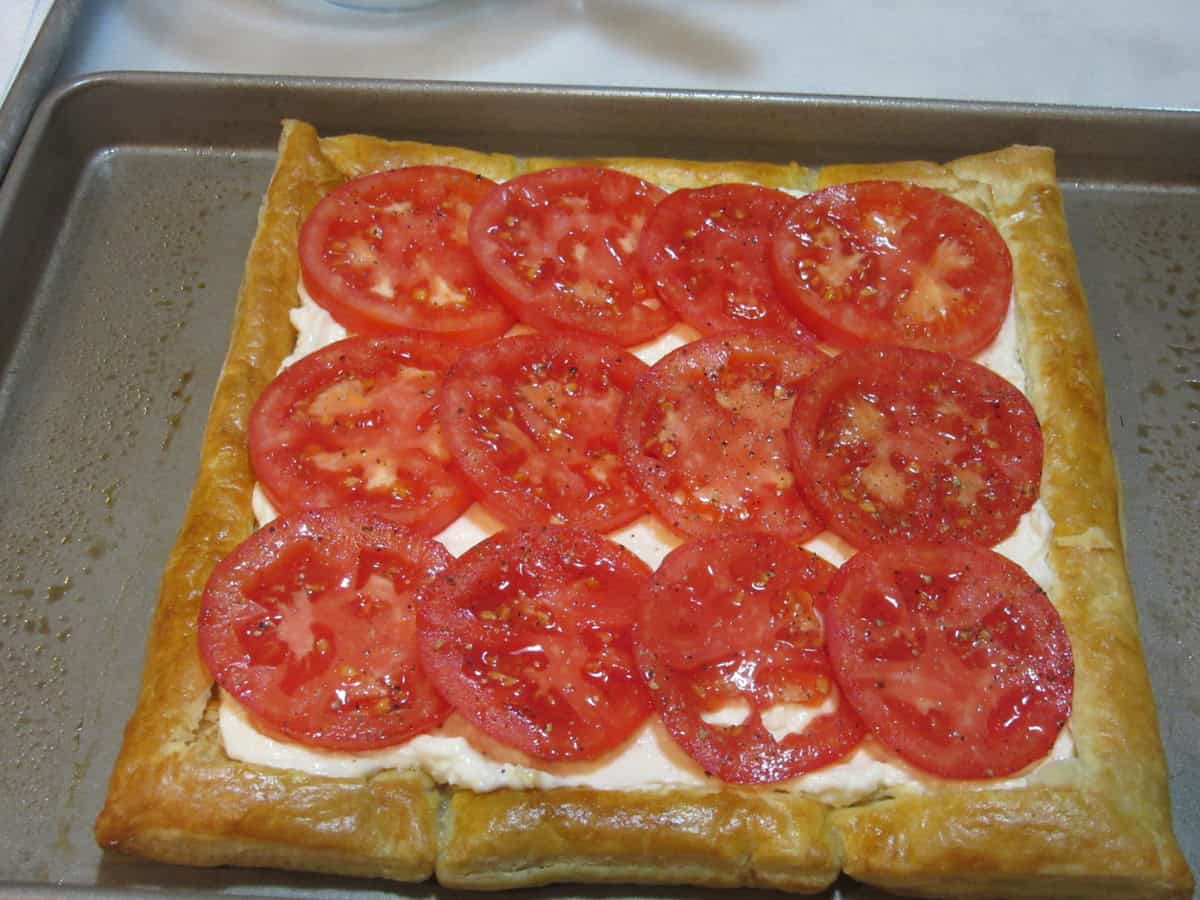 Seasoned tomato slices lined up in the center of a baked puff pastry sheet.