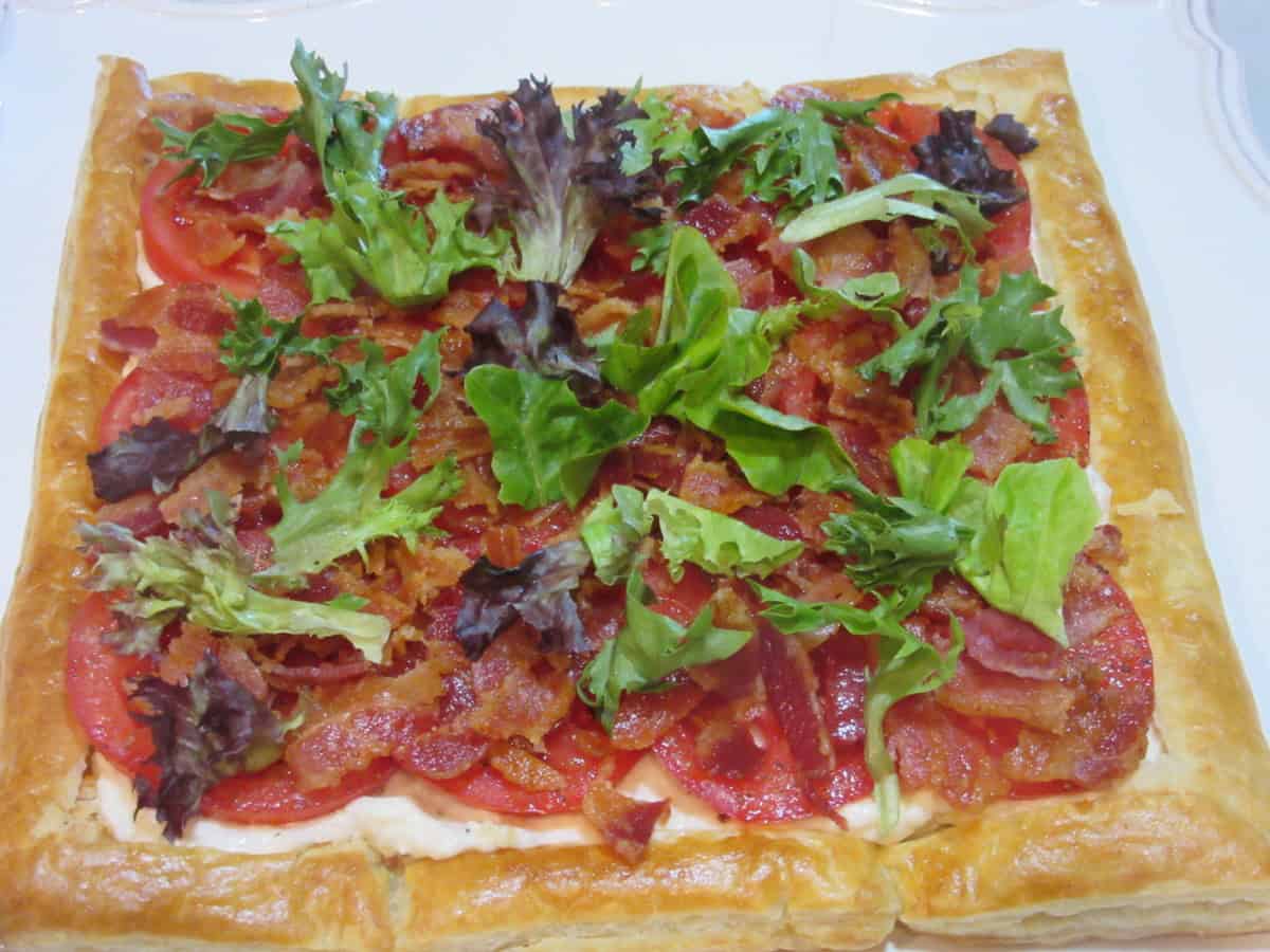 A spring mix of lettuces spread over a puff pastry bacon and tomato tart.