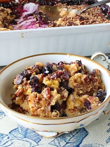 A pretty dish with a serving of cake mix blueberry crisp on a blue and white tablecloth.