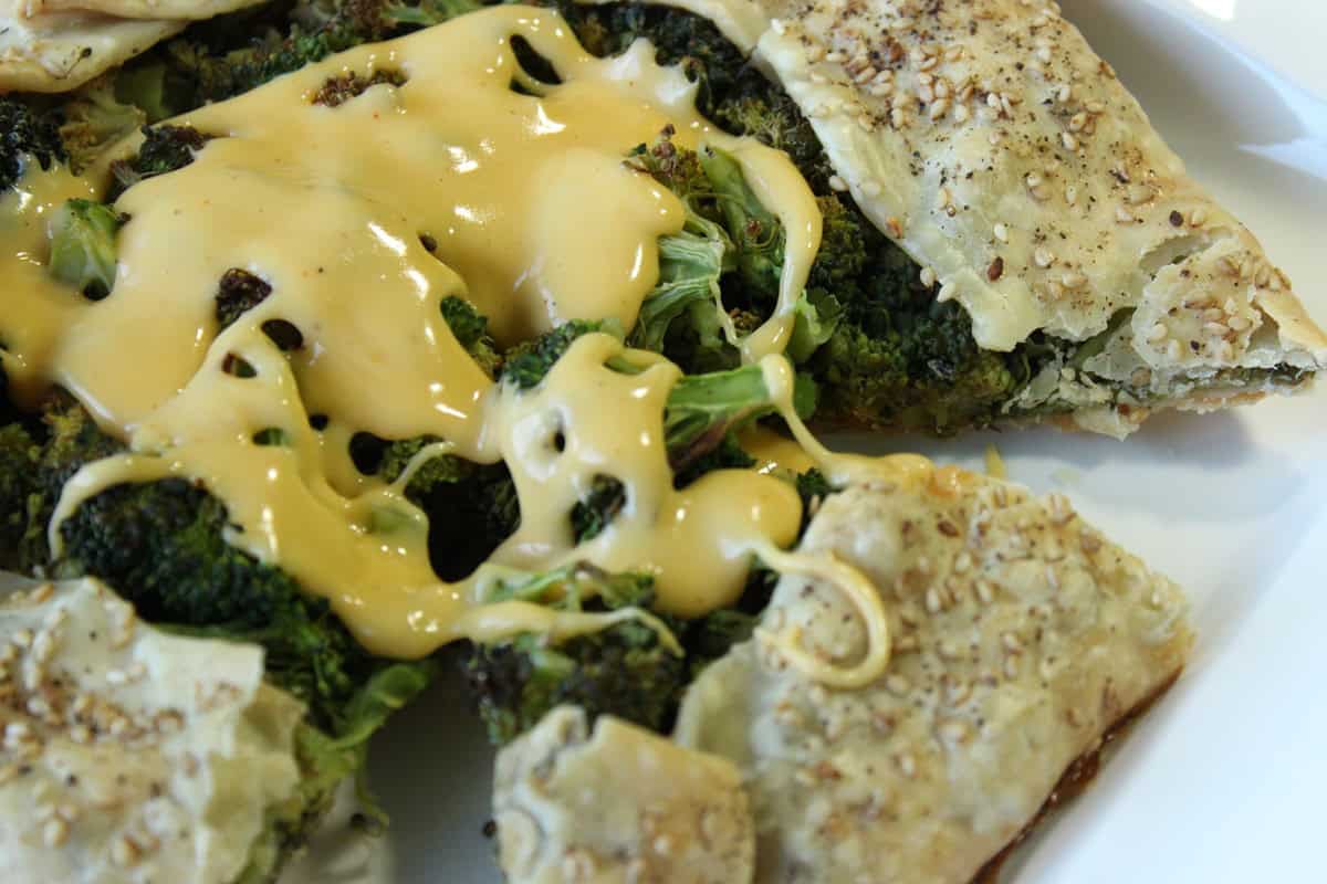 Roasted Broccoli Crostata with Cheese Sauce is a fun and unique new way to serve (and eat) your vegetables. - Kudos Kitchen by Renee A closeup look at a cheesy topped broccoli crostata with a sesame seed coating on the pie crust.