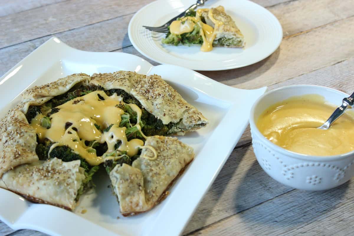 A square white plate holding a broccoli and cheese crostata with a slice removed.