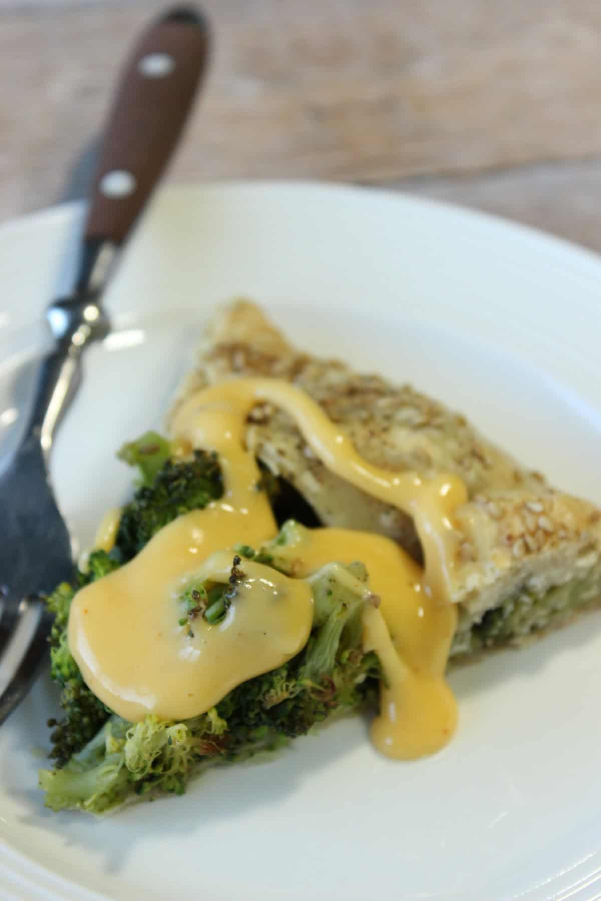 A slice of cheesy savory broccoli crostata on a white plate with a fork.