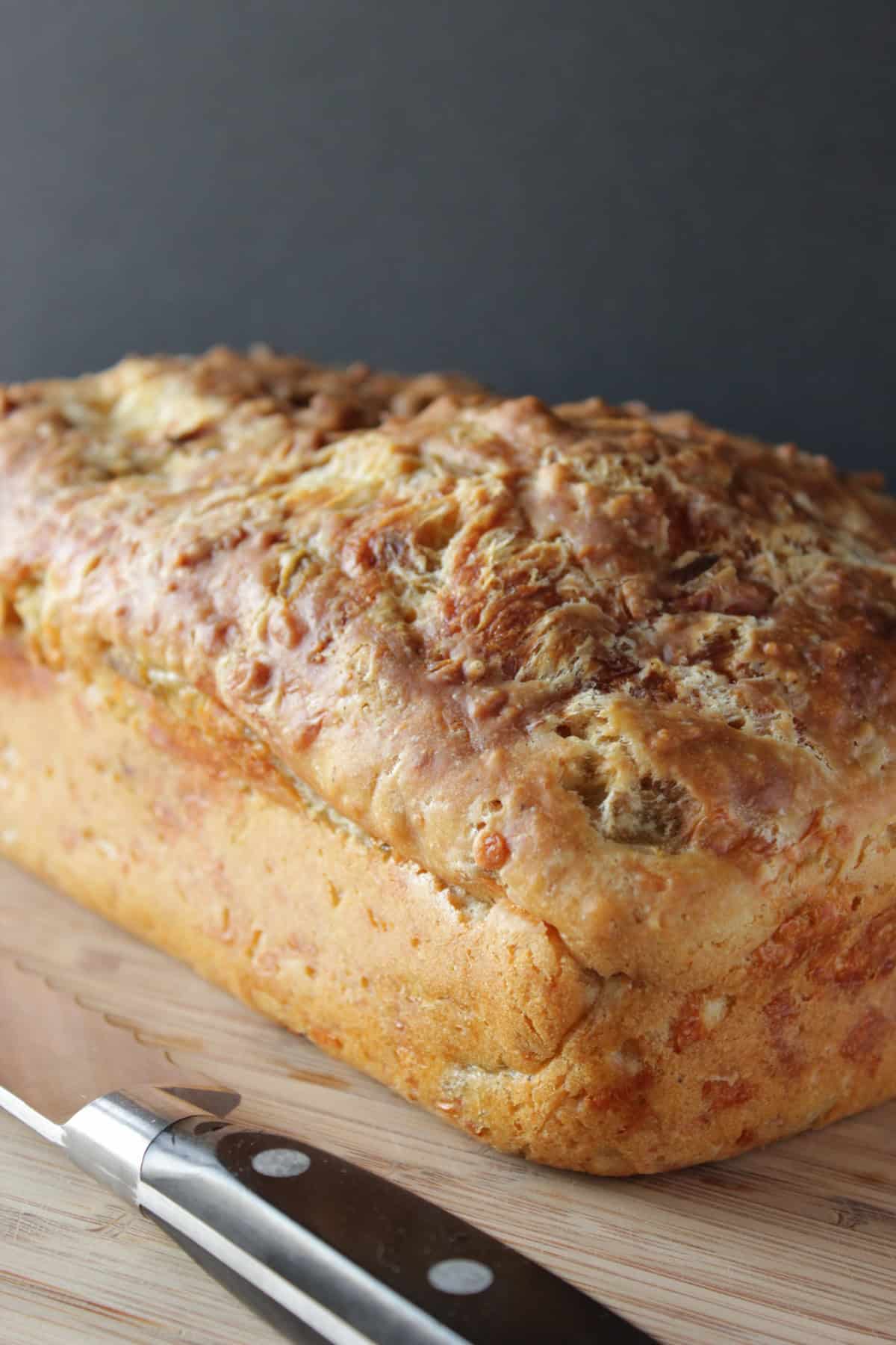 A golden brown crispy looking loaf of cheesy jalapeno quick bread on a wooden cutting board.