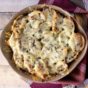 A round casserole dish filled with baked, cheese-topped French onion stuffed shells.