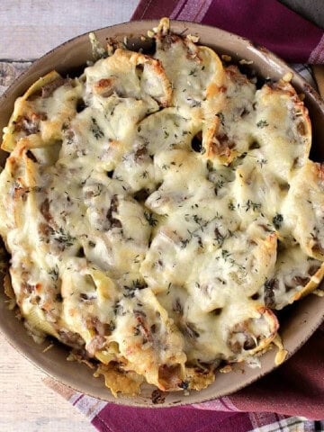 A round casserole dish filled with baked, cheese-topped French onion stuffed shells.