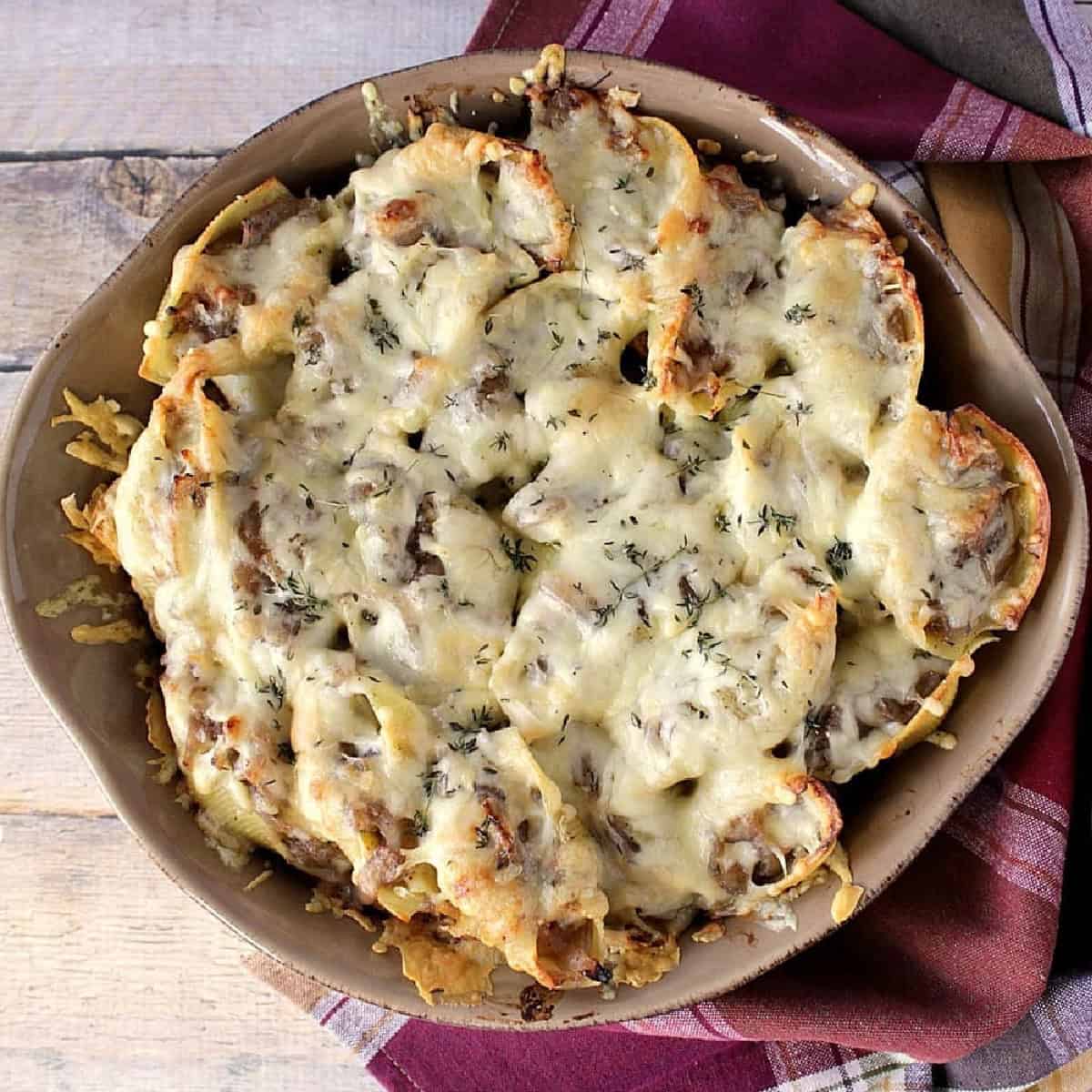 A round casserole dish filled with baked, cheese-topped French onion stuffed shells.