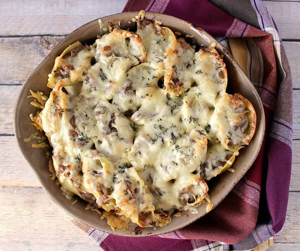A round casserole dish filled with cheese and thyme topped French onion stuffed shells.