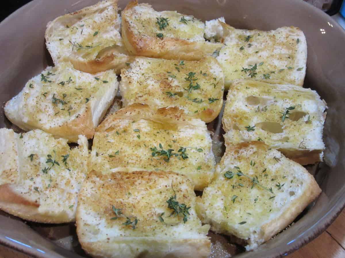 French bread cut in half and drizzled with olive oil and thyme leaves in a round casserole dish.