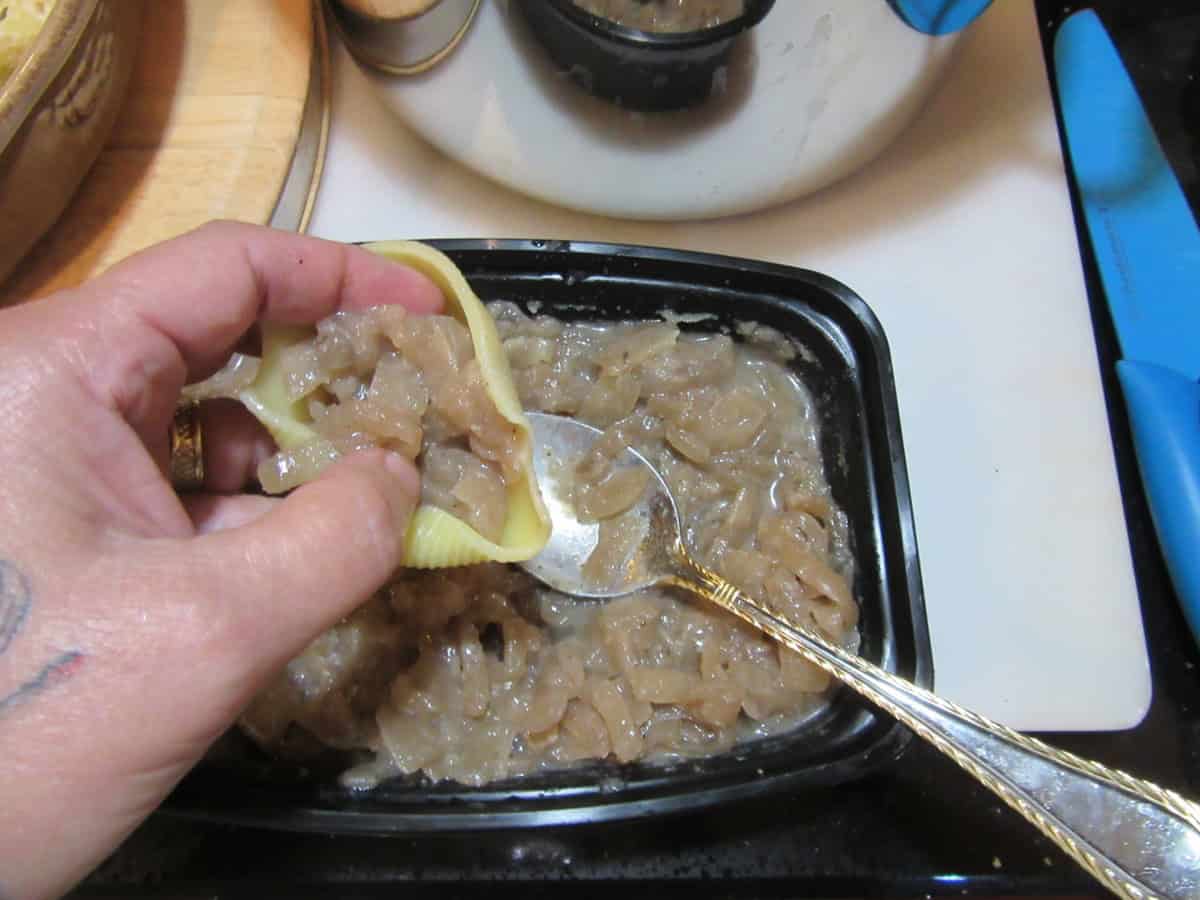 A hand stuffing cooked red wine onions into cooked pasta shells.