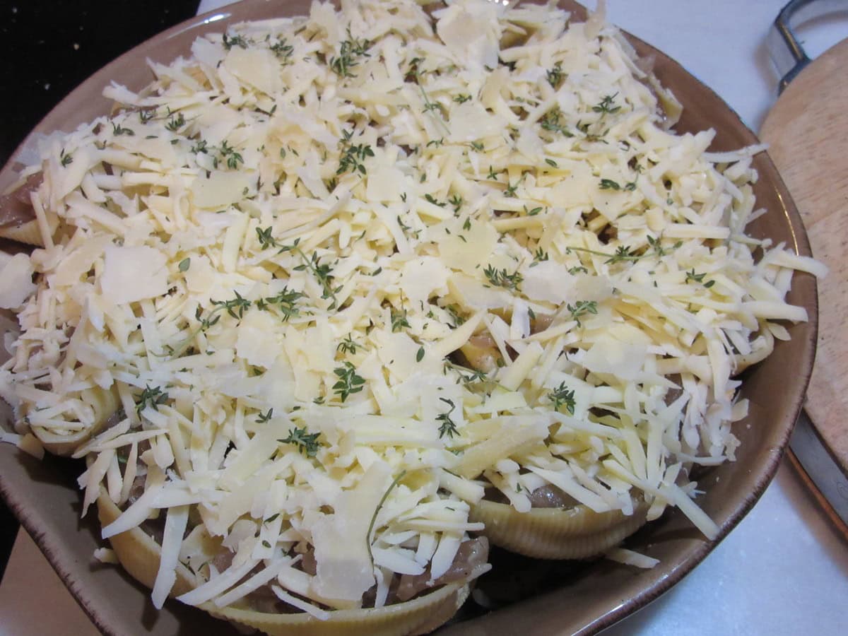 Shredded Swiss cheese on top of a casserole dish filled with onion stuffed shells.