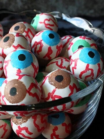 Blue, brown, and green eyeball gumballs in a glass bowl for Halloween.
