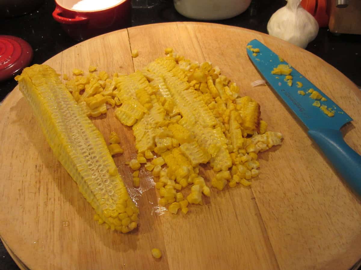 A blue knife on a cutting board after cutting kernels off and ear of corn.