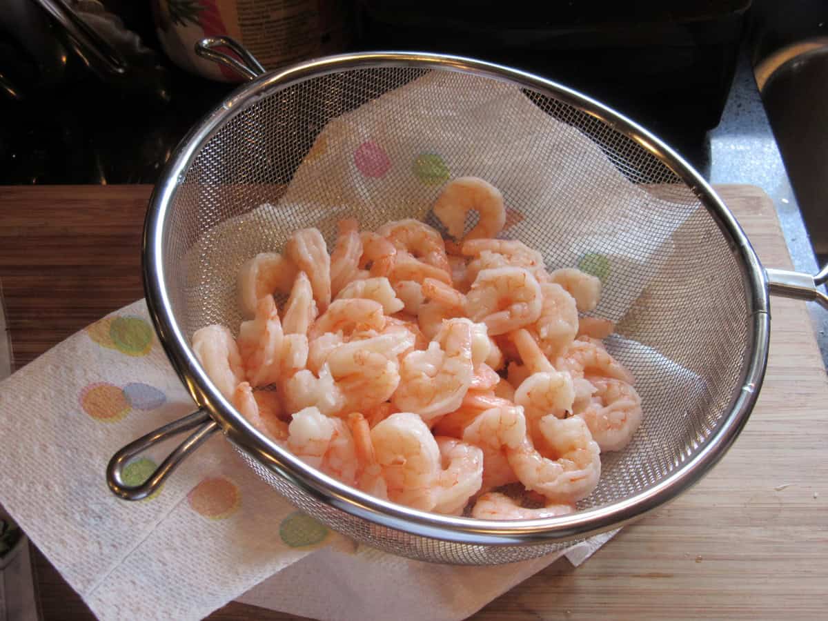 A colander with cooked shrimp inside after being rinsed.