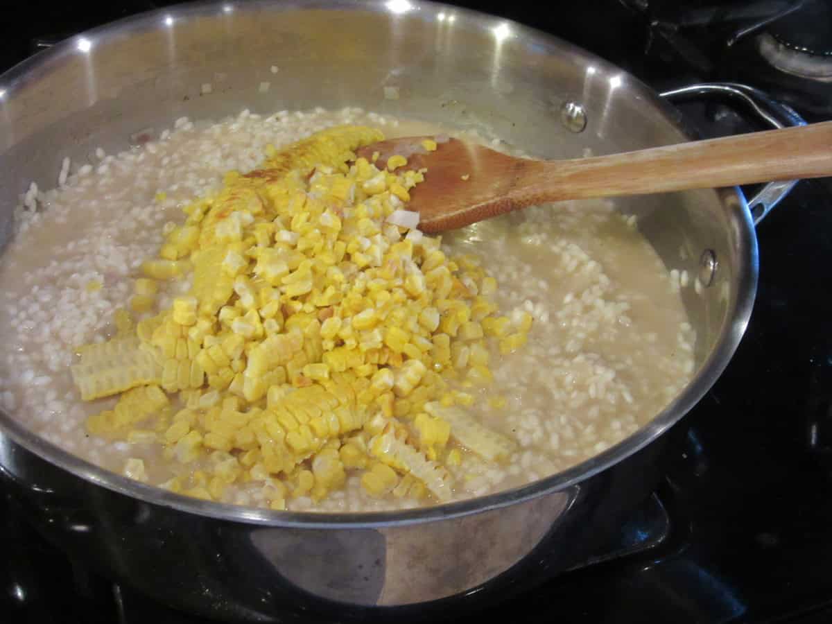 Roasted corn kernels added to a skillet with arborio rice and chicken broth.