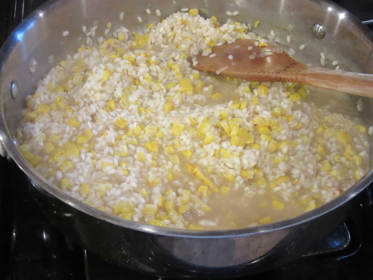 A skillet with arborio rice, corn, and chicken broth for making risotto.