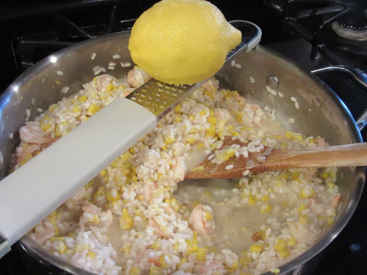 A fresh lemon being zested into a skillet of shrimp risotto.