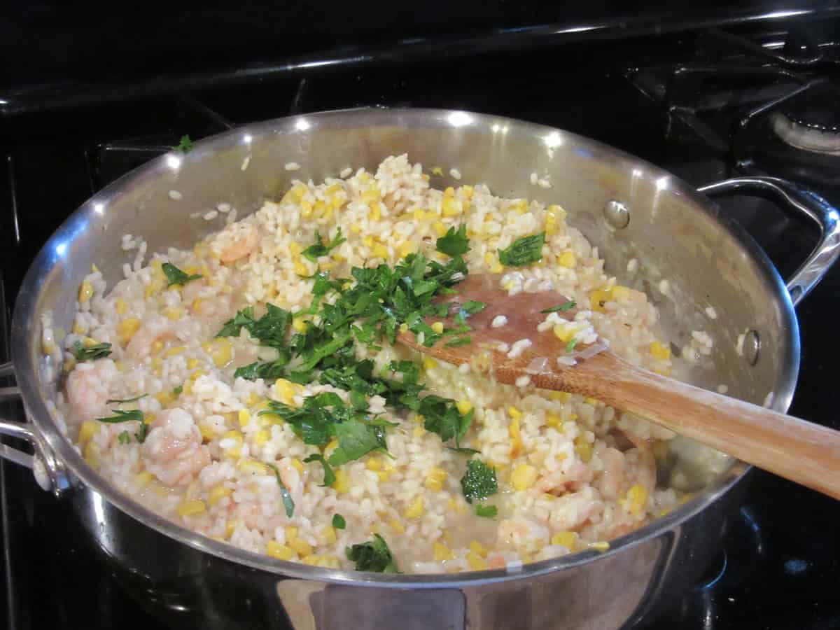 Chopped parsley added to a skillet with shrimp risotto.