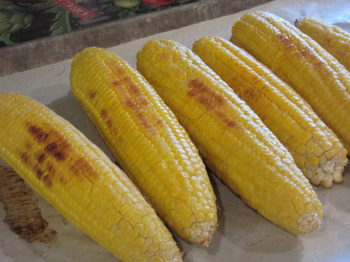 Ears of roasted corn on a baking sheet with parchment paper.