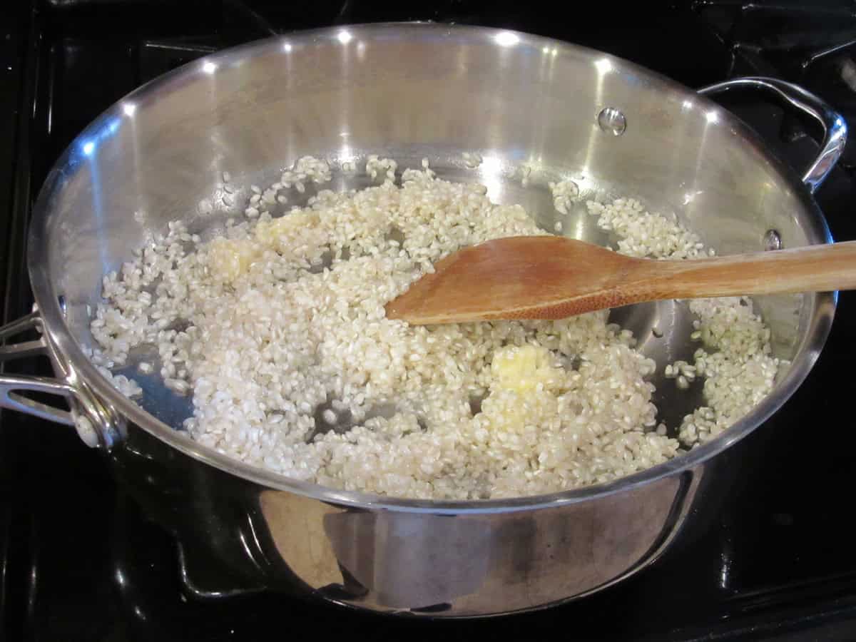 Arborio rice and butter in a large silver skillet for making risotto.