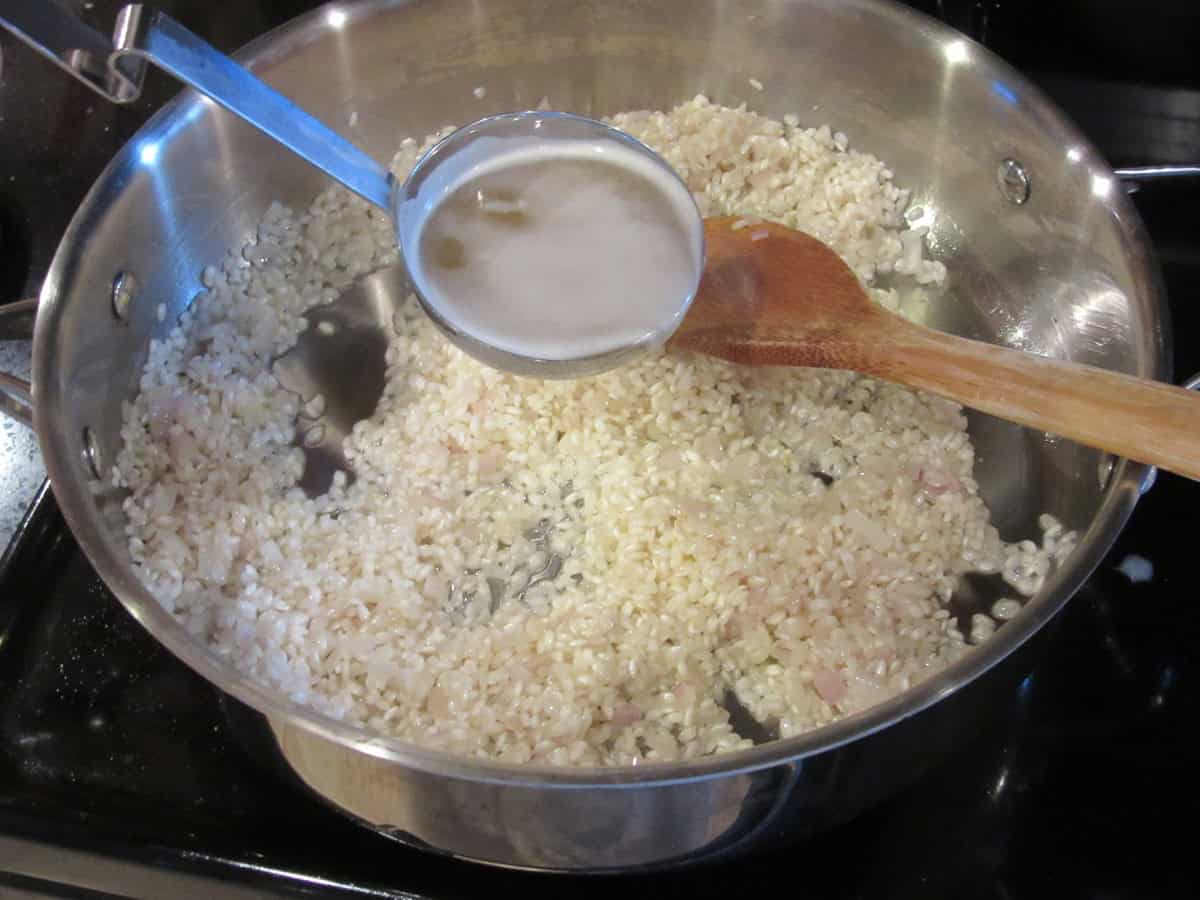 Arborio rice and shallots in a skillet while hot chicken broth is being added.