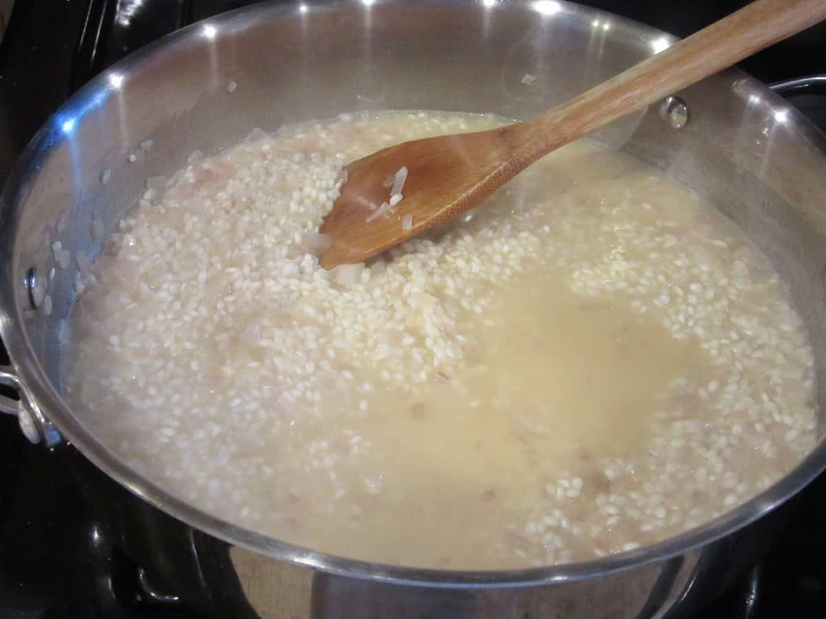 Arborio rice in a skillet with chicken broth and a wooden spoon.