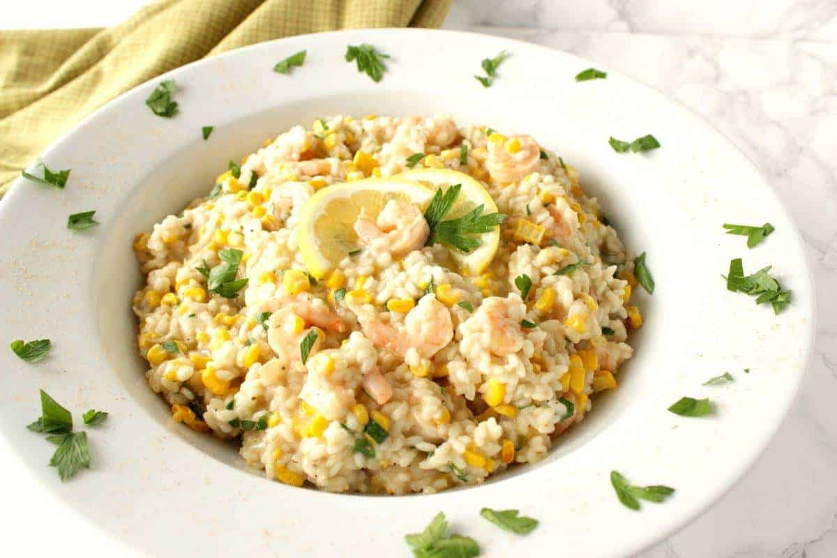 New England Sweet Corn Risotto is a great way to use up the last of summer's bounty of sweet corn. It's a creamy and delicious main course that can be on the dinner table in approximately 30 minutes. - Kudos Kitchen by Renee - kudoskitchenbyrenee.com A pretty bowl or sweet corn and shrimp risotto with parsley around the side ready for dinner.