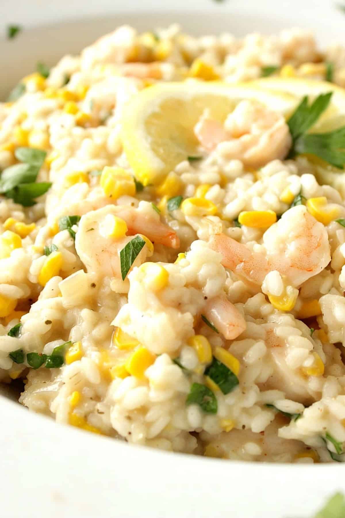 A creamy looking sweet corn and shrimp risotto topped with lemon slices and parsley.