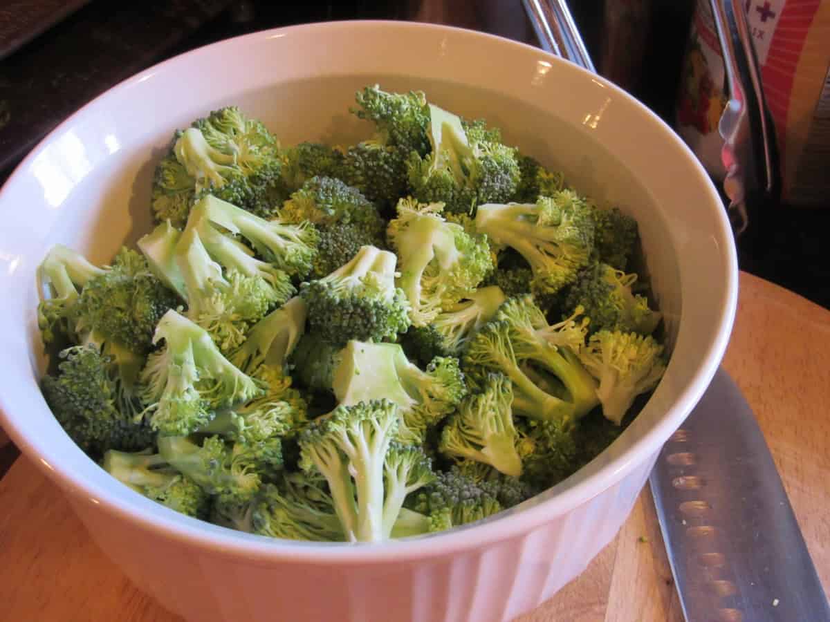 Uncooked chopped broccoli florets in a white round casserole dish.