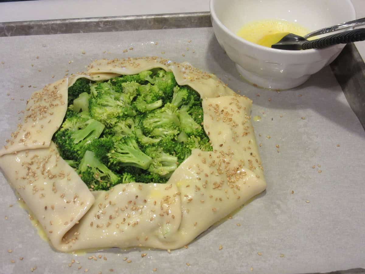 A broccoli crostata before baking on a parchment lined baking sheet.