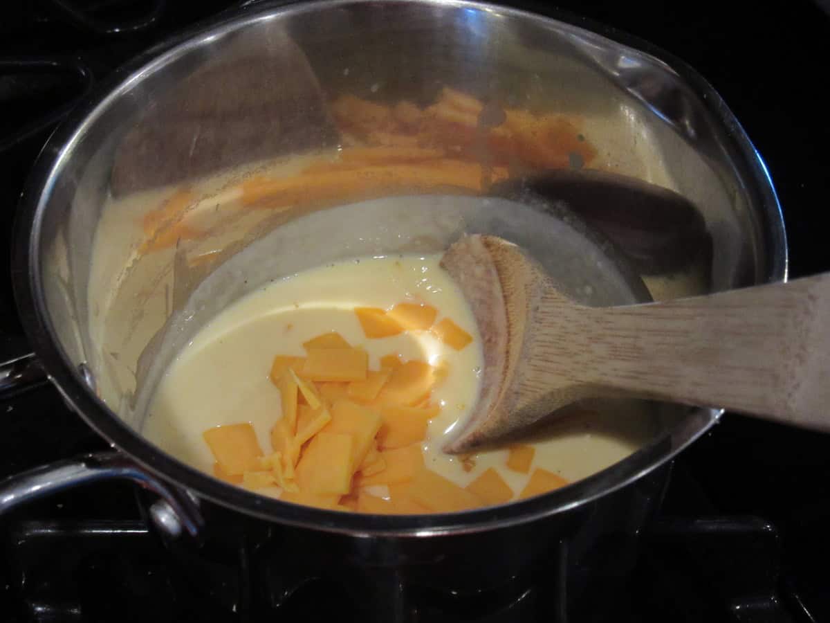 Cheese cubes in a saucepan with a wooden spoon and cheese sauce.