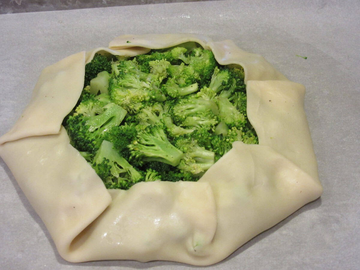 Folded edges of pie crust surrounding cooked broccoli on a baking sheet.