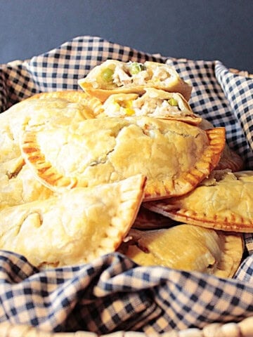 A basket filled with chicken pot pie hand pies and a black and tan napkin.