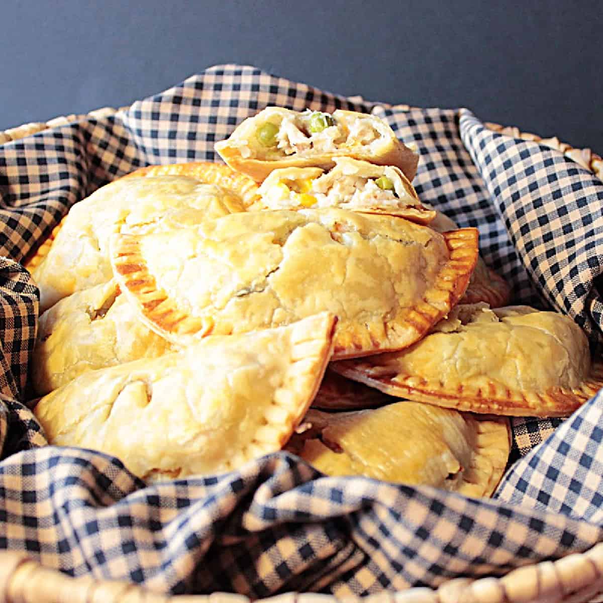 A basket filled with chicken pot pie hand pies and a black and tan napkin.