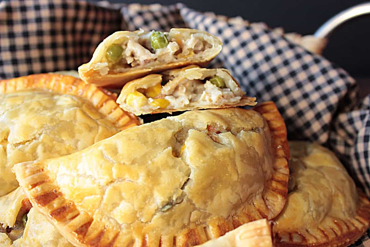 A basket full of chicken pot pie hand pies with one being open to see what's inside.