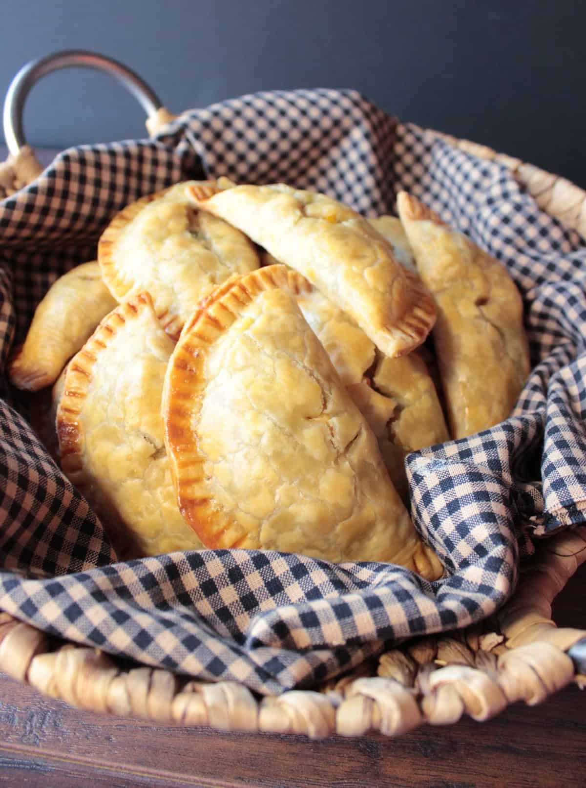 A bunch of golden brown chicken pot pie pockets in a basket with a brown and tan cloth napkin.