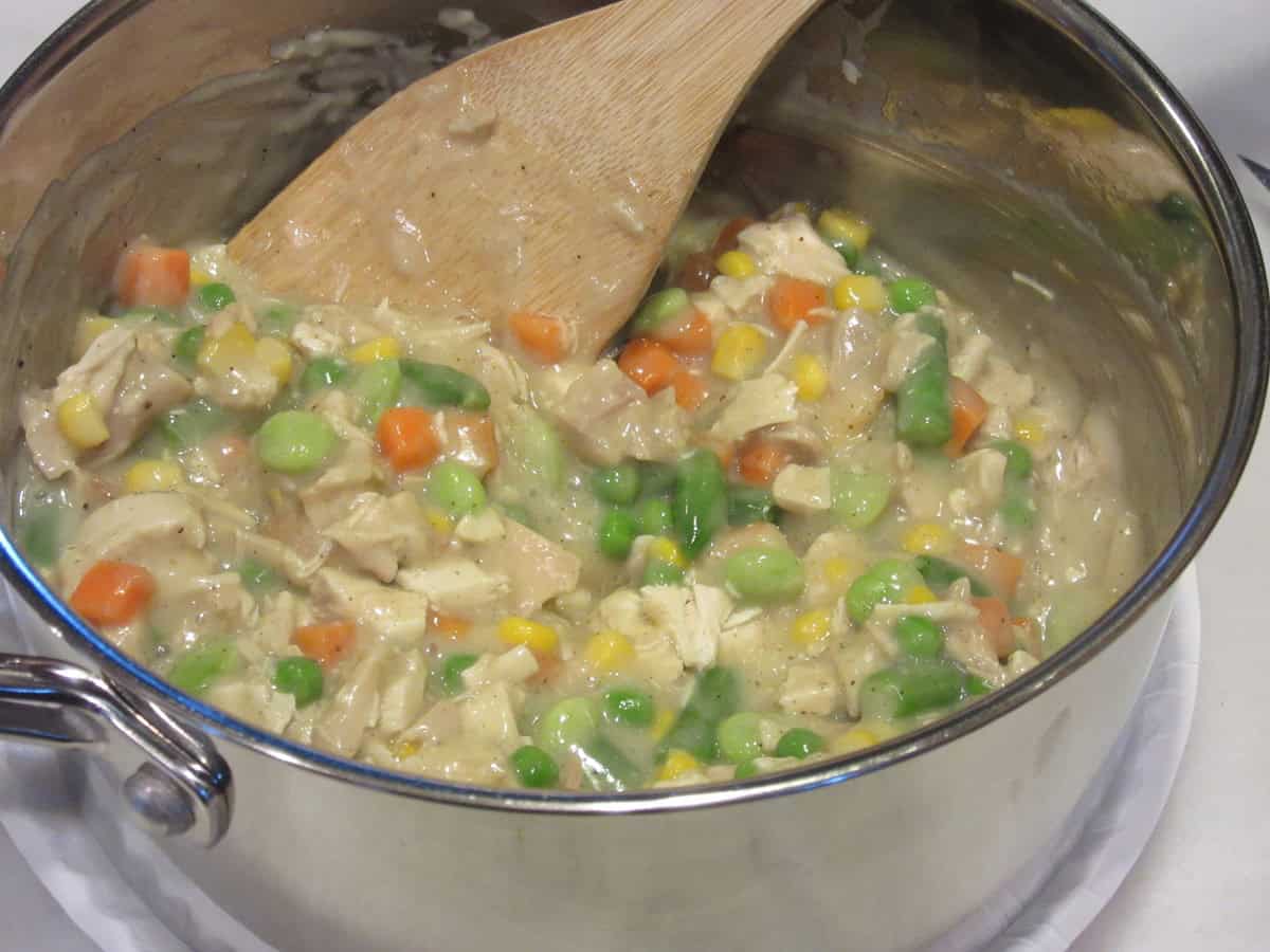 A chicken pot pie filling mixture in a saucepan with a wooden spoon.