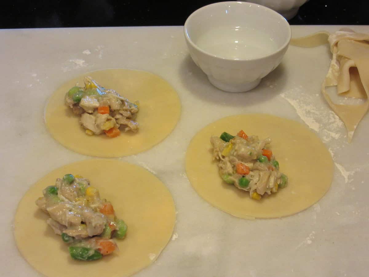 Three small pie crust rounds with chicken pot pie filling on one side of each crust.