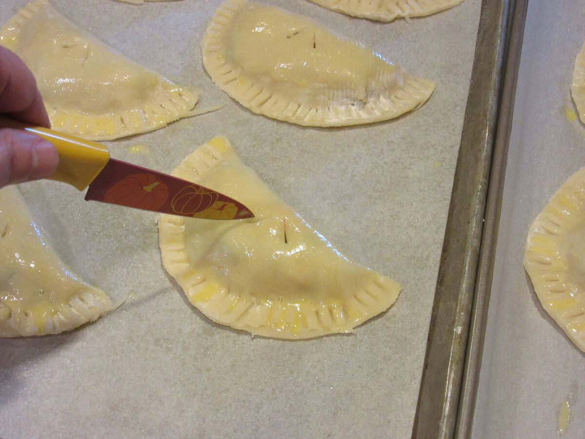 A paring knife adding vent holes to the tops of chicken pot pie crust pockets.